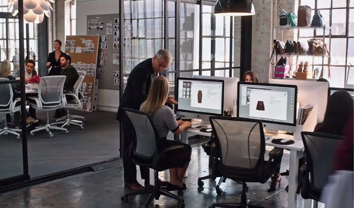 two people working on computers in an office with lots of glass walls and floor to ceiling windows