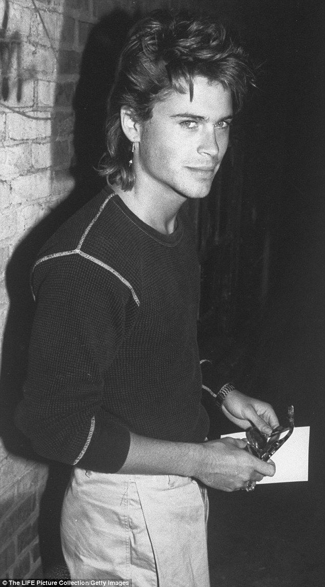 a young man standing next to a brick wall holding a piece of paper and scissors