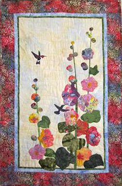 a quilted wall hanging with flowers and birds in the sky on it's side