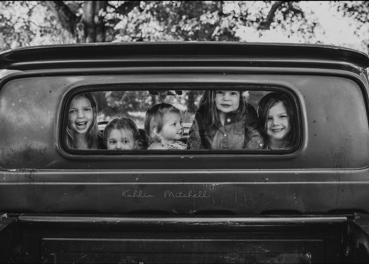 six children are looking out the window of an old truck