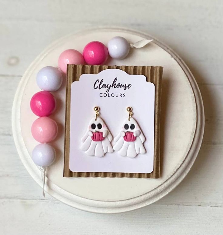 two pairs of earrings with pink and white beads on top of a plate next to some balloons