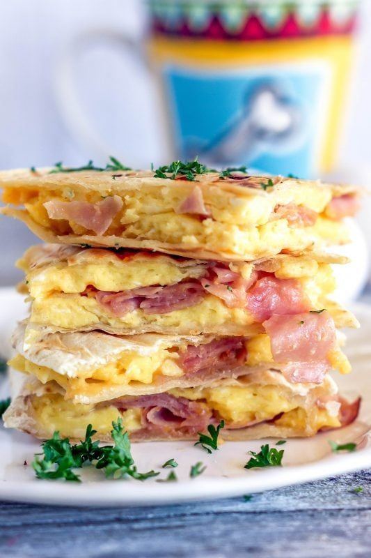 a stack of eggs, ham and cheese pancakes on a plate next to a cup