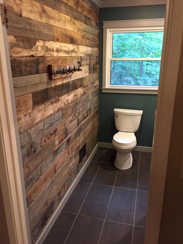 a white toilet sitting in a bathroom next to a wooden paneled wall and window