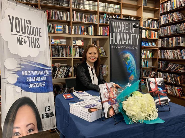 a woman sitting at a table in front of a book shelf with books on it