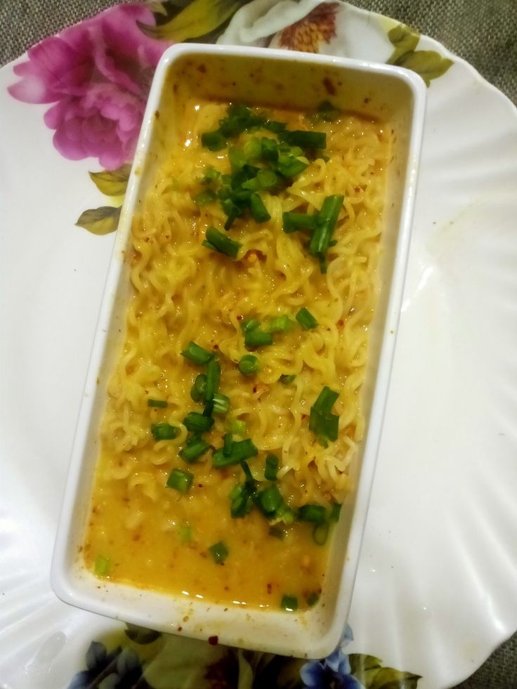 a white dish filled with noodles and green onions on top of a flowered plate