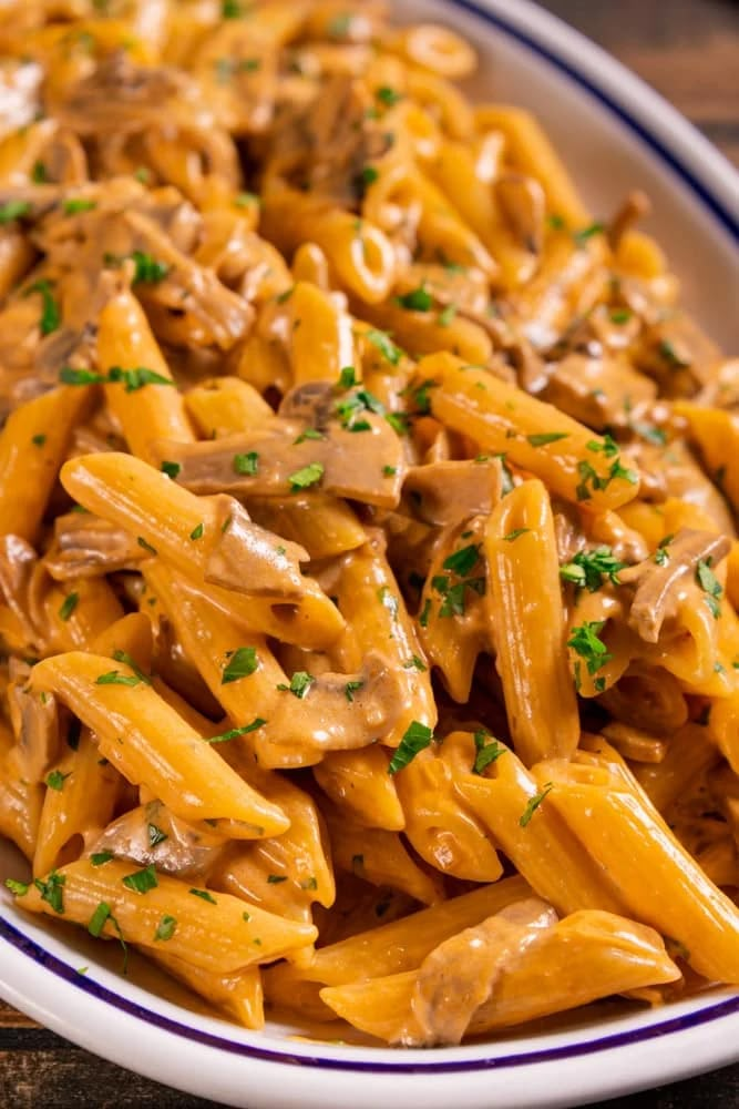 pasta with mushroom sauce and parsley in a white bowl on a wooden table top