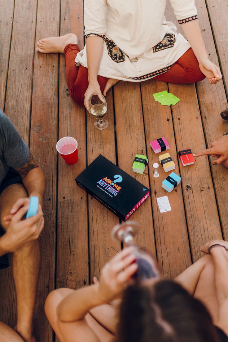 three people sitting on the ground playing with their cell phones and drinking from plastic cups