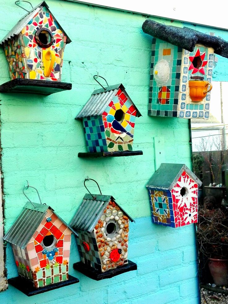 colorful birdhouses are hanging on the side of a blue brick wall in front of a potted plant