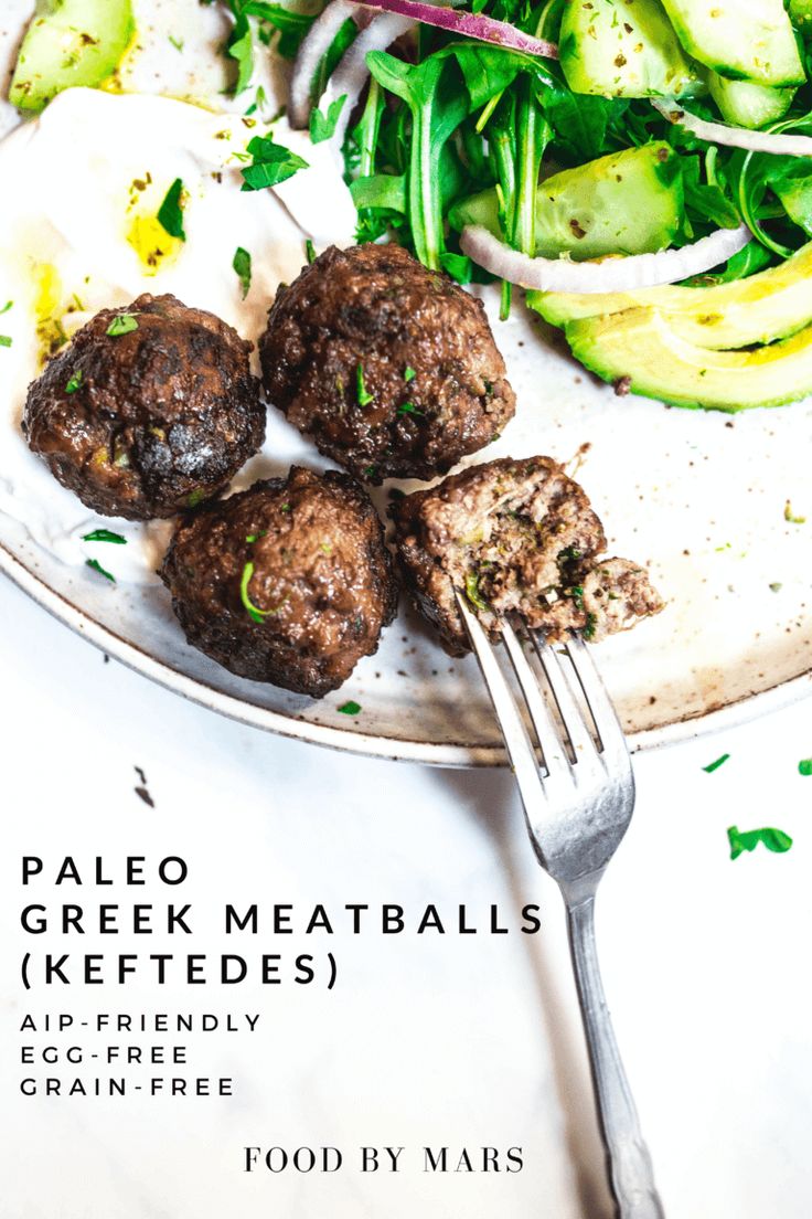 a white plate topped with meatballs next to a green salad and cucumbers