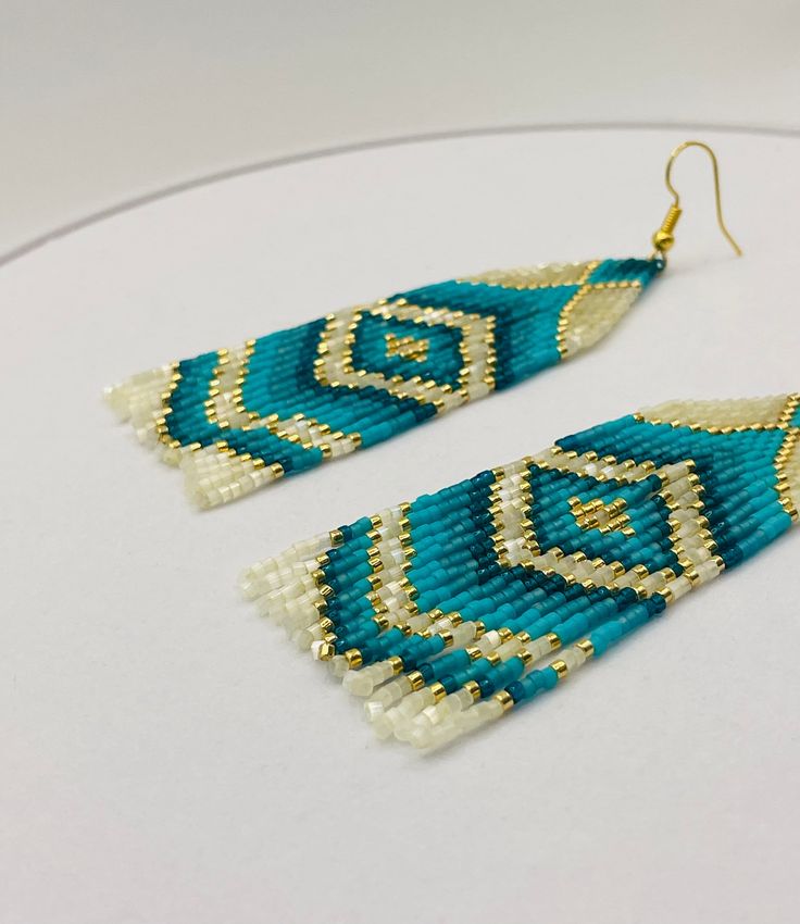 a pair of blue and white beaded earrings sitting on top of a round table