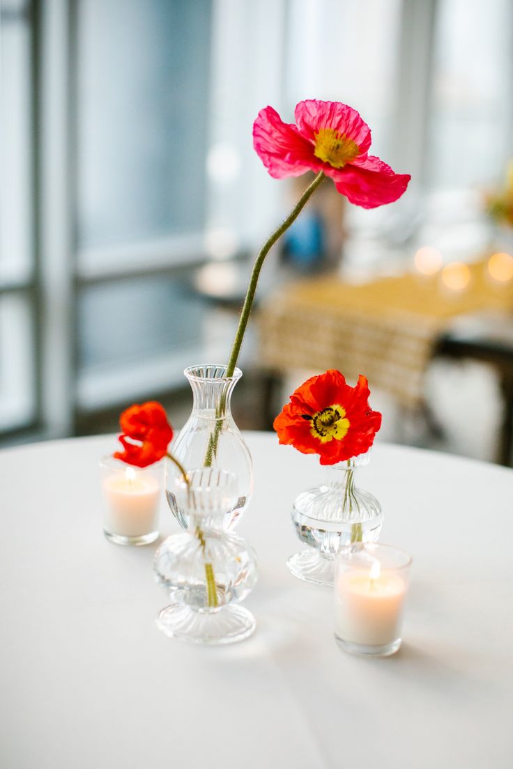 three vases filled with flowers on top of a white tablecloth covered dining room table