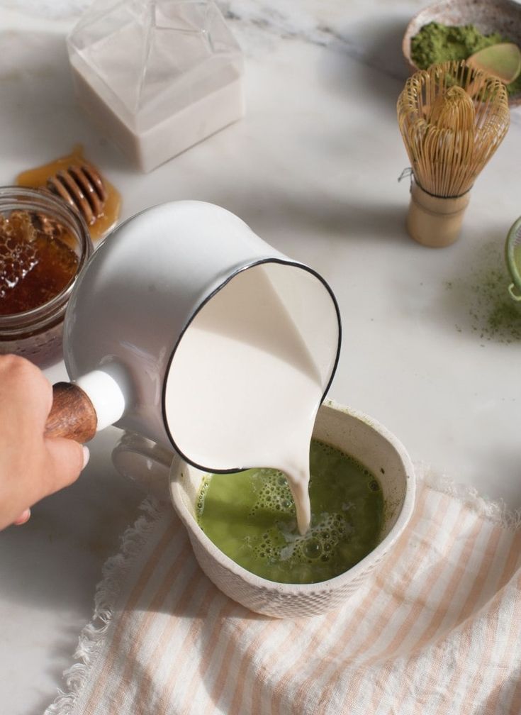 a person pours green liquid into a cup on a table with other dishes and utensils