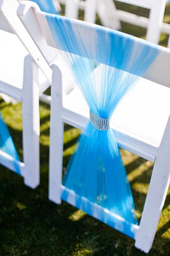 two white chairs with blue sashes on them sitting in the grass near each other