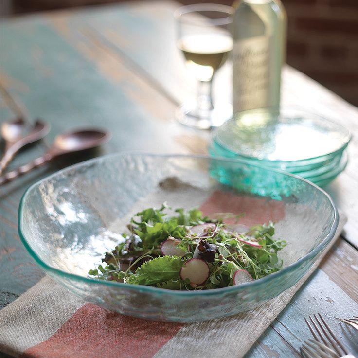 a glass bowl filled with salad on top of a wooden table next to a bottle of wine