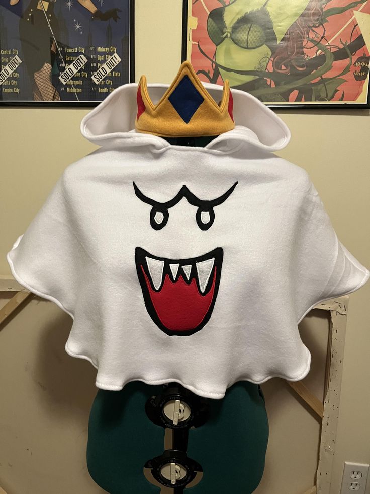 a white t - shirt with a crown on it's head is displayed in front of two posters