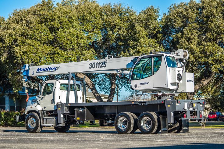 a white truck with a crane on it's back in front of some trees