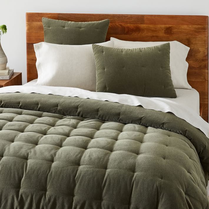 a bed with green comforter and pillows on it