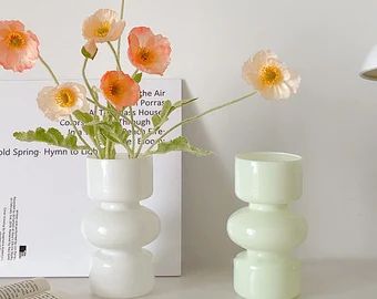 a white vase with flowers in it sitting on a table next to an open book