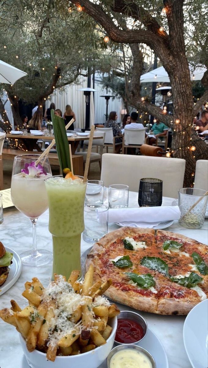 a table topped with plates of food next to a glass of juice and a pizza