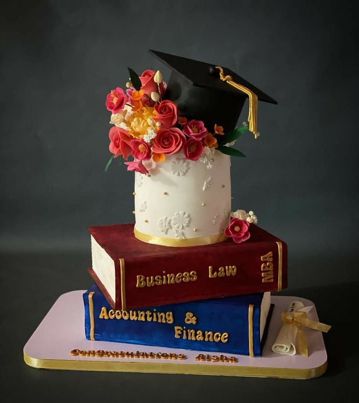 there is a cake that has flowers on top of it and books in the shape of a graduate's hat