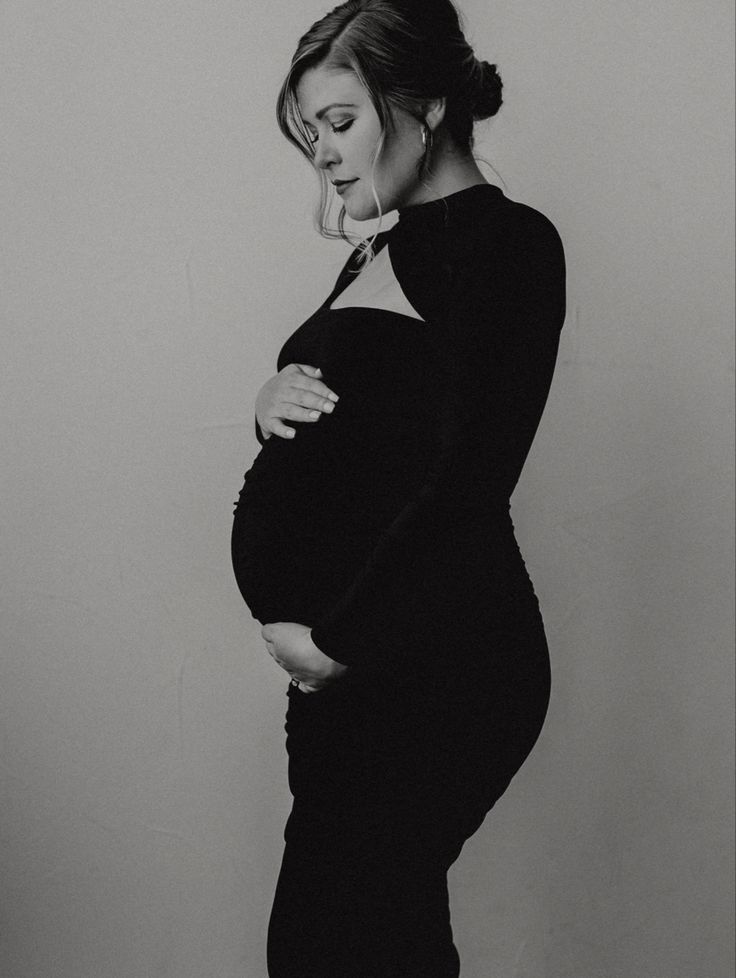 a pregnant woman poses for a black and white photo with her hand on her belly