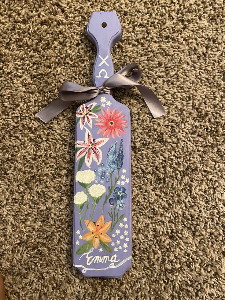 a purple bottle with flowers painted on it sitting on the floor next to a pair of scissors