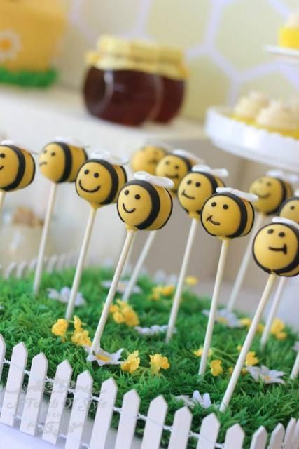 there are many cake pops that have been placed in the grass with bees on them