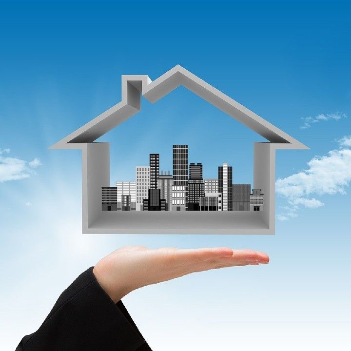 a person's hand holding out a house shaped like a building with the sky in the background