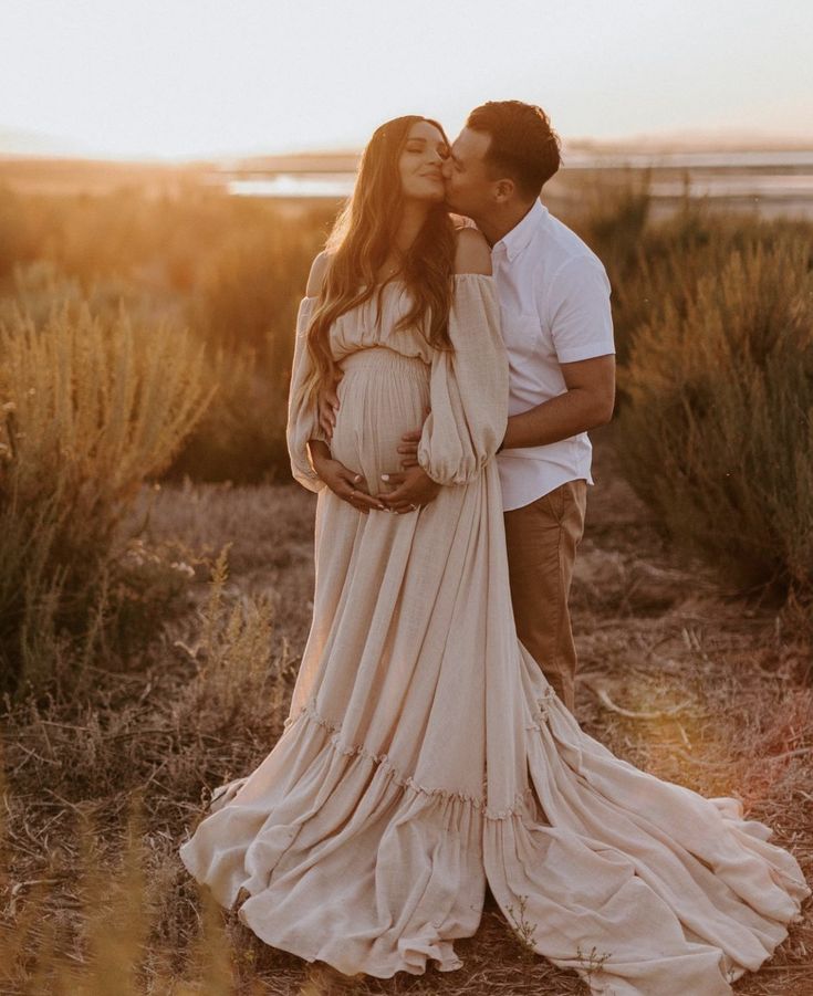 a pregnant couple kissing in the desert at sunset with their baby bumping her belly