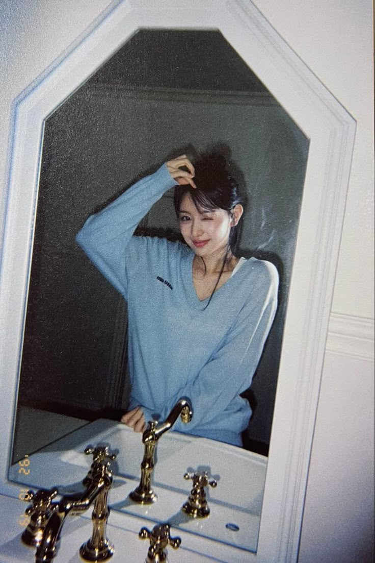 a woman is standing in front of a mirror with her hands on her head and looking into the mirror