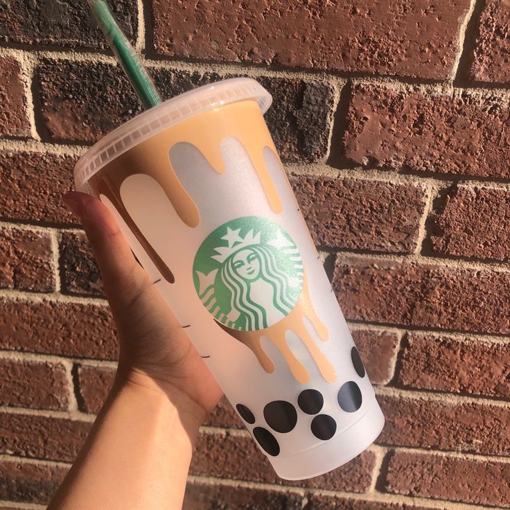 a hand holding up a starbucks cup in front of a brick wall with polka dots on it