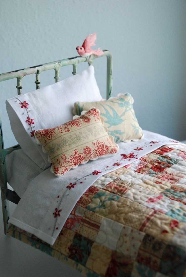 a bed topped with lots of pillows next to a white wall and a pink bird on top of the headboard