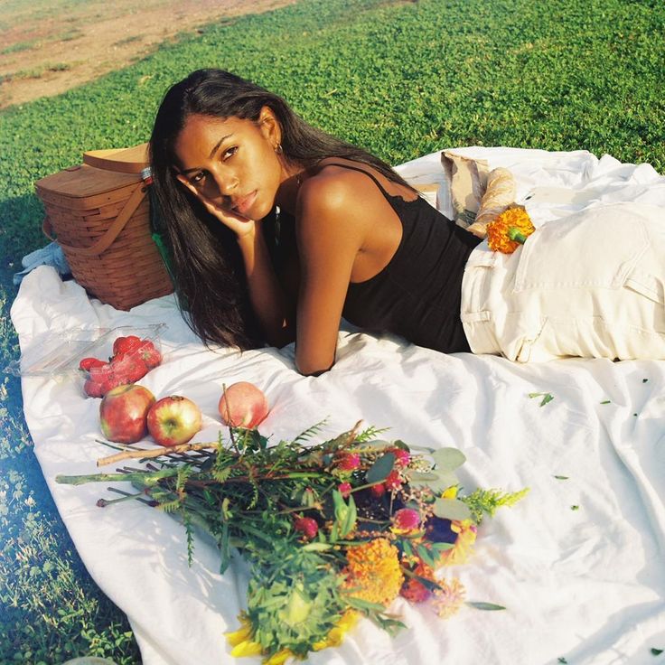 a woman laying on a blanket in the grass with apples and flowers next to her