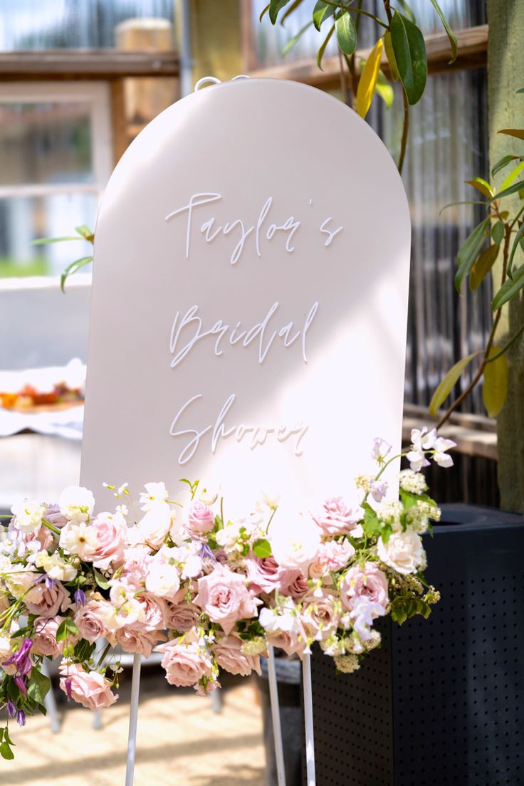 a white sign with writing on it sitting next to flowers