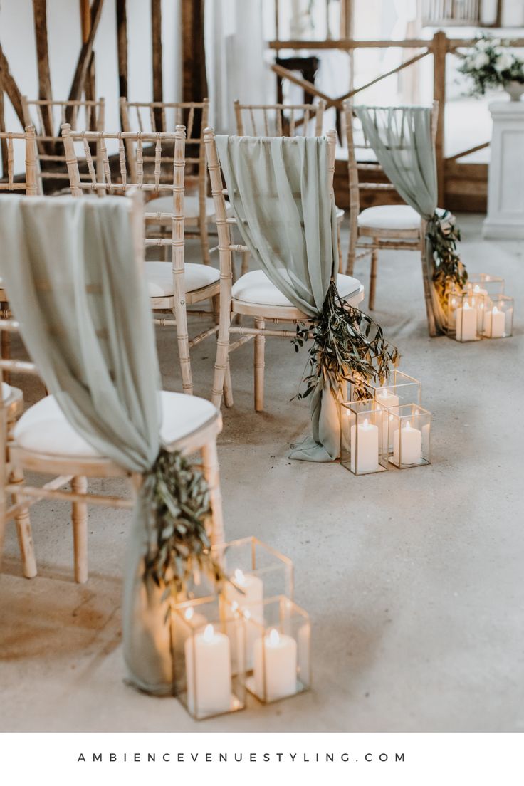 candles are lit in front of chairs with drapes draped over them and decorated with greenery