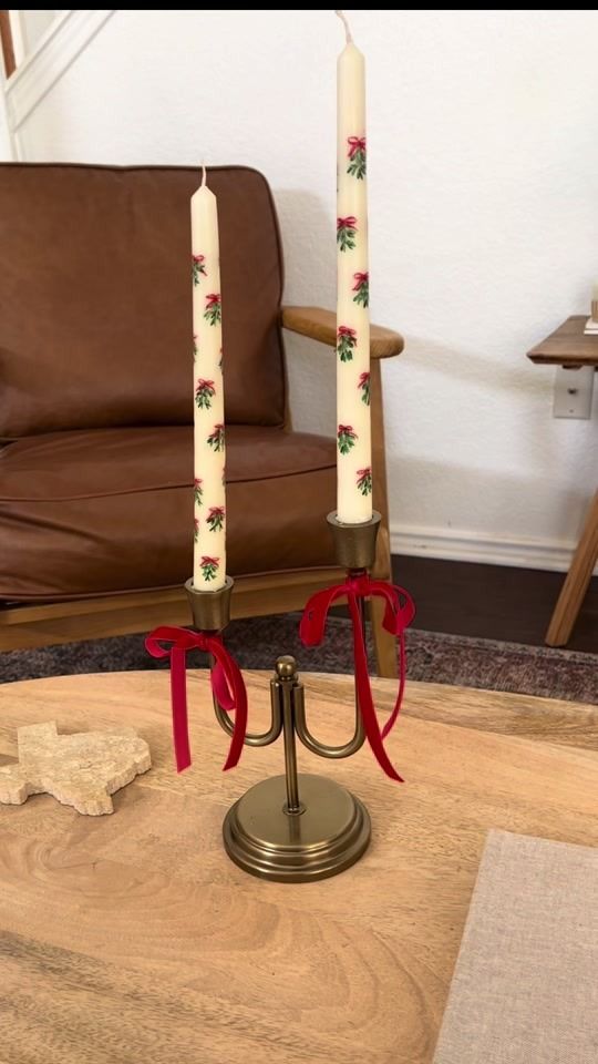 two candles are sitting on a table with red ribbon around them and one candle is lit