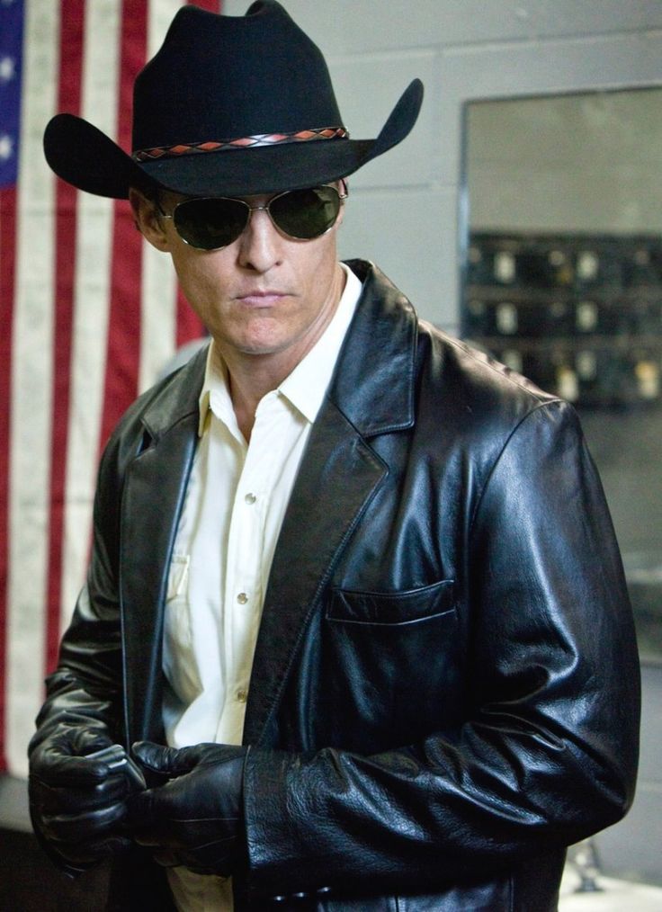 a man in a leather jacket and cowboy hat is holding his hands on his hip