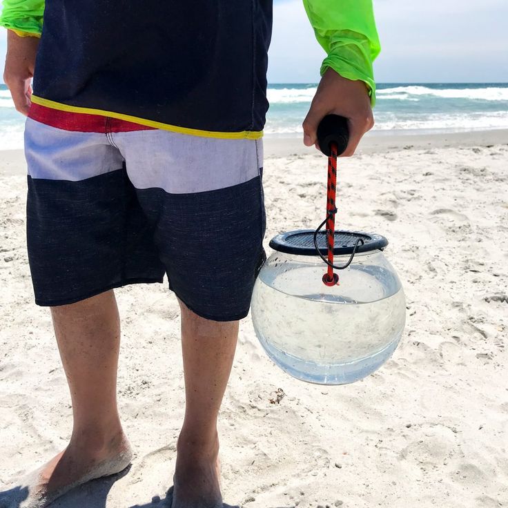 a man standing on top of a sandy beach next to the ocean holding an object in his hand