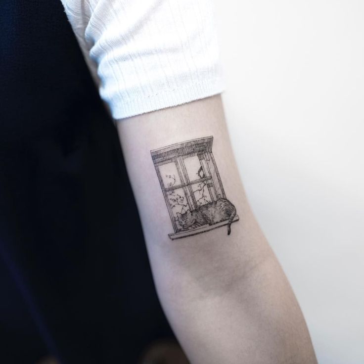 a person with a small tattoo on their arm that has an image of a cat in a window