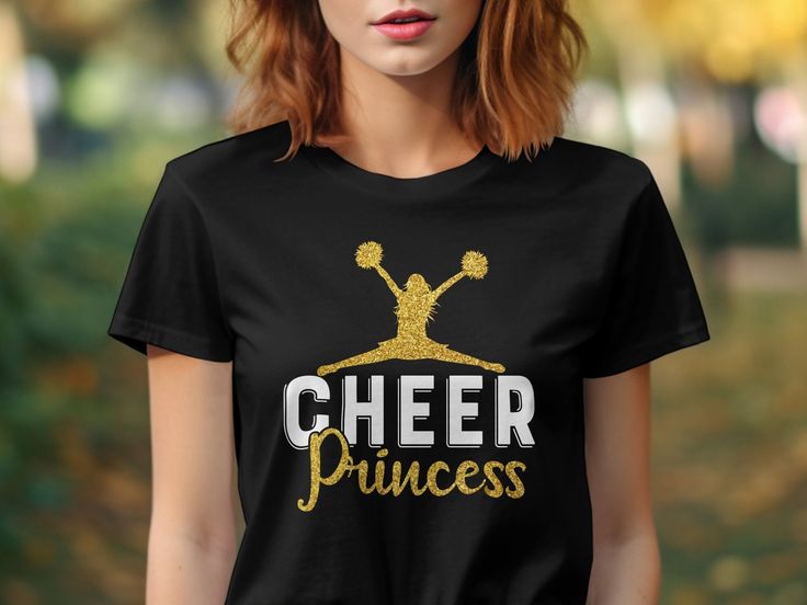 Elevate your cheerleading wardrobe with our Cheer Princess Cheerleading T-Shirt. This tee features a striking glitter graphic design that stands out, making it perfect for cheer squad members. Ideal for practice, game day, or casual wear, it represents style and team spirit. Whether you're a cheerleader or a supportive fan, this shirt is a must-have for showcasing your love for cheerleading.  The Gildan 5000 t-shirt features a medium-weight 100% cotton fabric with no side seams for a seamless fi Graphic Tee T-shirt For Cheerleading, Cheerleading Fan Apparel Tops With Sublimation Print, Team Spirit Tops With Sublimation Print For Cheerleading, Cheerleading Graphic Print Fan Apparel Tops, Crew Neck T-shirt With Sublimation Print For Cheerleading, Casual Glitter Print Tops For Cheerleading, Black Sublimation Print T-shirt For Cheerleading, Black T-shirt With Sublimation Print For Cheerleading, Black Short Sleeve Tops For Cheerleading