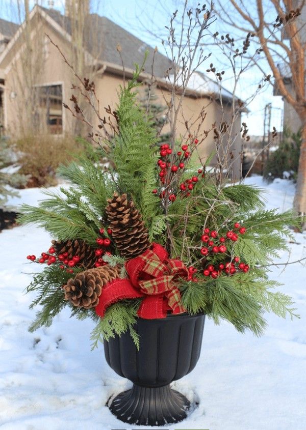 a potted plant in the snow with pine cones, berries and evergreens on it