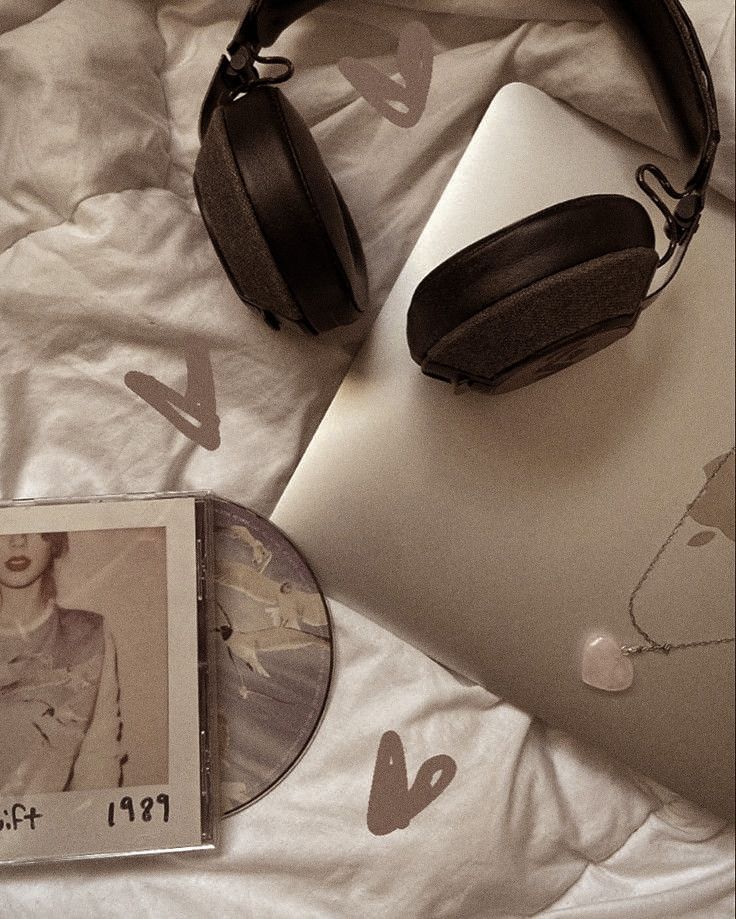 an open laptop computer sitting on top of a bed next to headphones and a cd