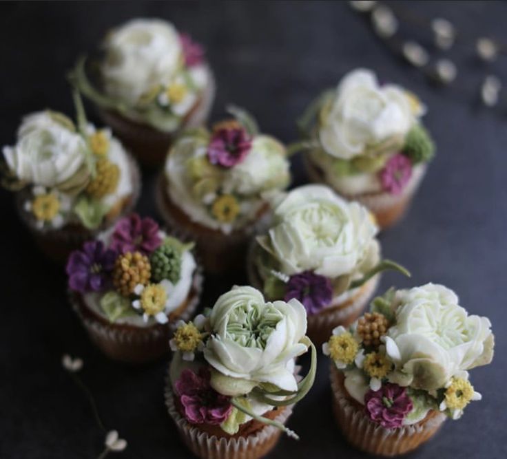 cupcakes decorated with white and purple flowers on a black table top, next to dried baby's breath buds