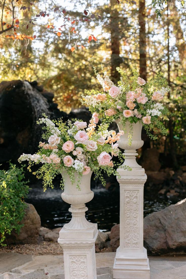 two tall white vases with flowers in them