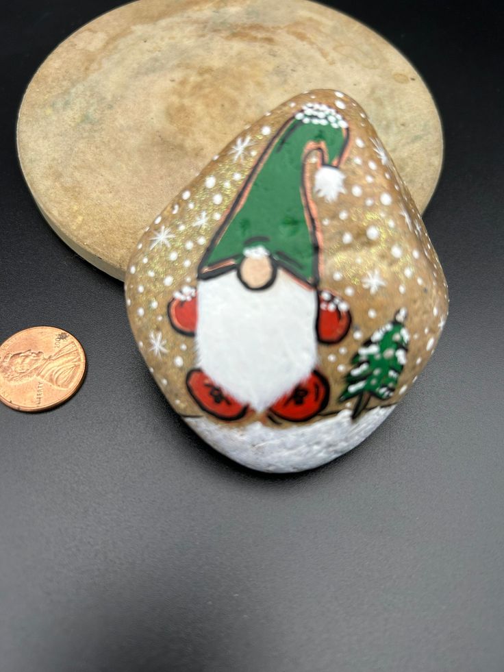 a rock with a gnome painted on it next to a penny