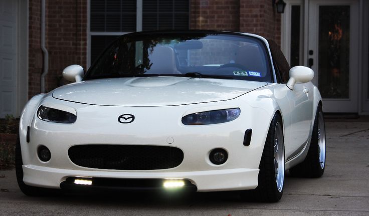 a white sports car is parked in front of a house with its hood up and lights on