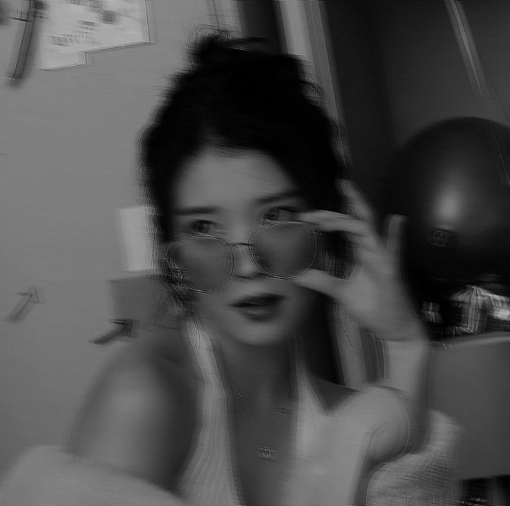 a black and white photo of a woman holding up her eyeglasses to the camera