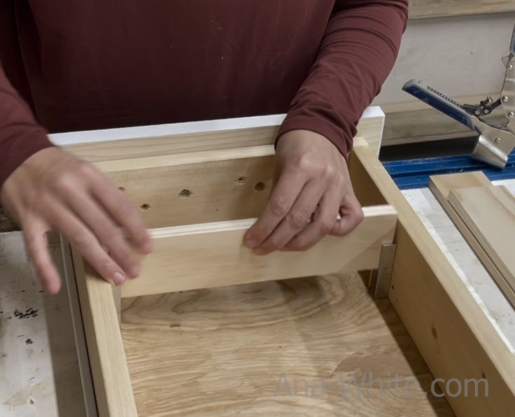 a man is working on some wood in his workshop, with one hand reaching for the top