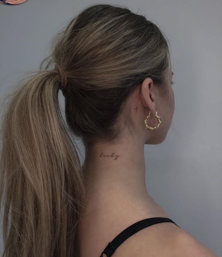 the back of a woman's head with a small tattoo on her left ear