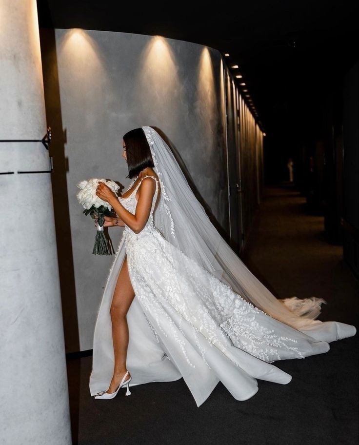 a woman in a wedding dress is walking down the hall with her bouquet and veil on